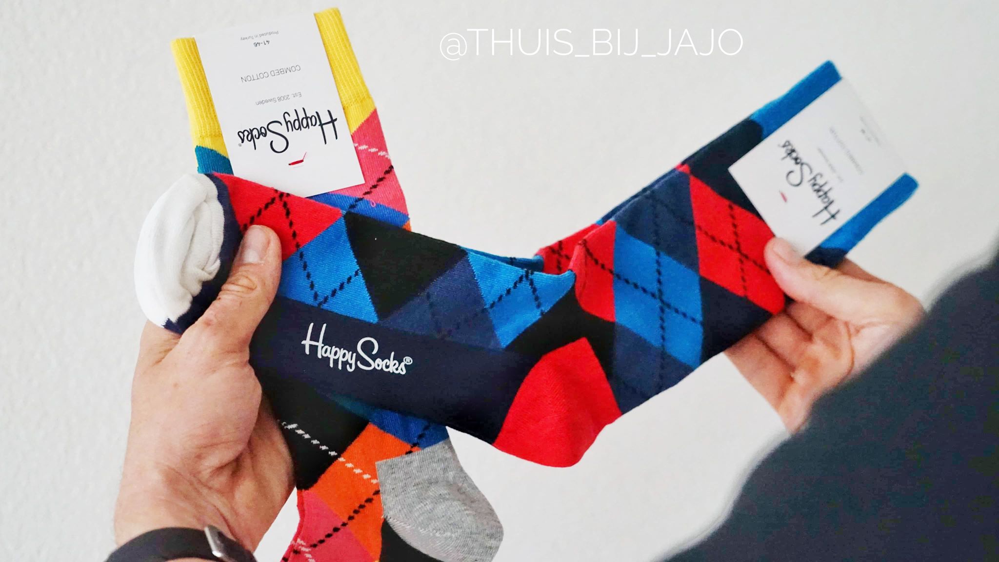 In de handen van mijn man zie je een paar happysocks in de kleuren rood blauw & roze geel oranje. 